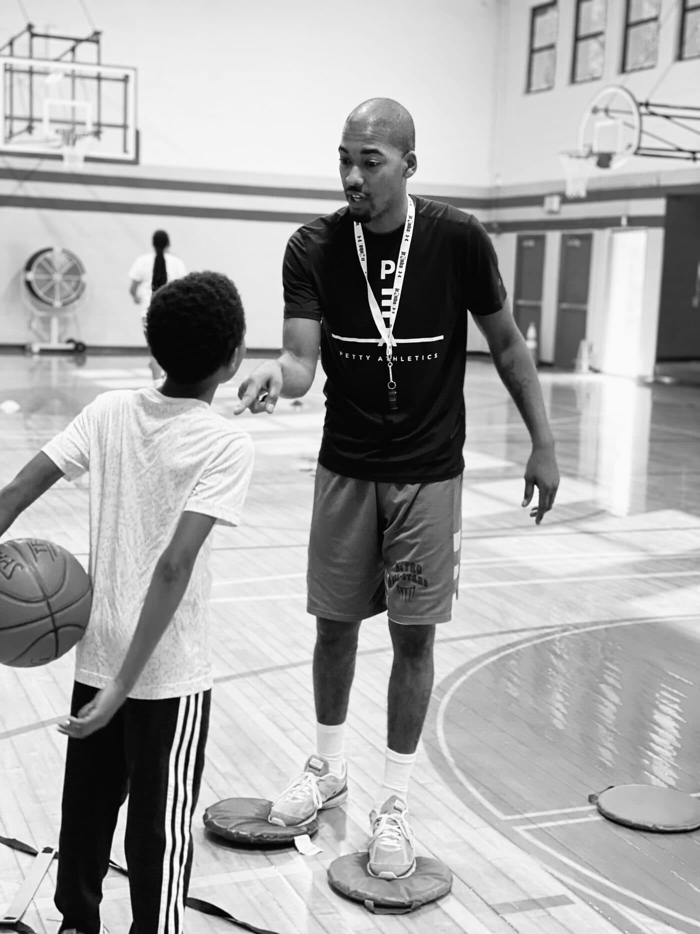 A coach walking alongside a young player who is holding a basketball
