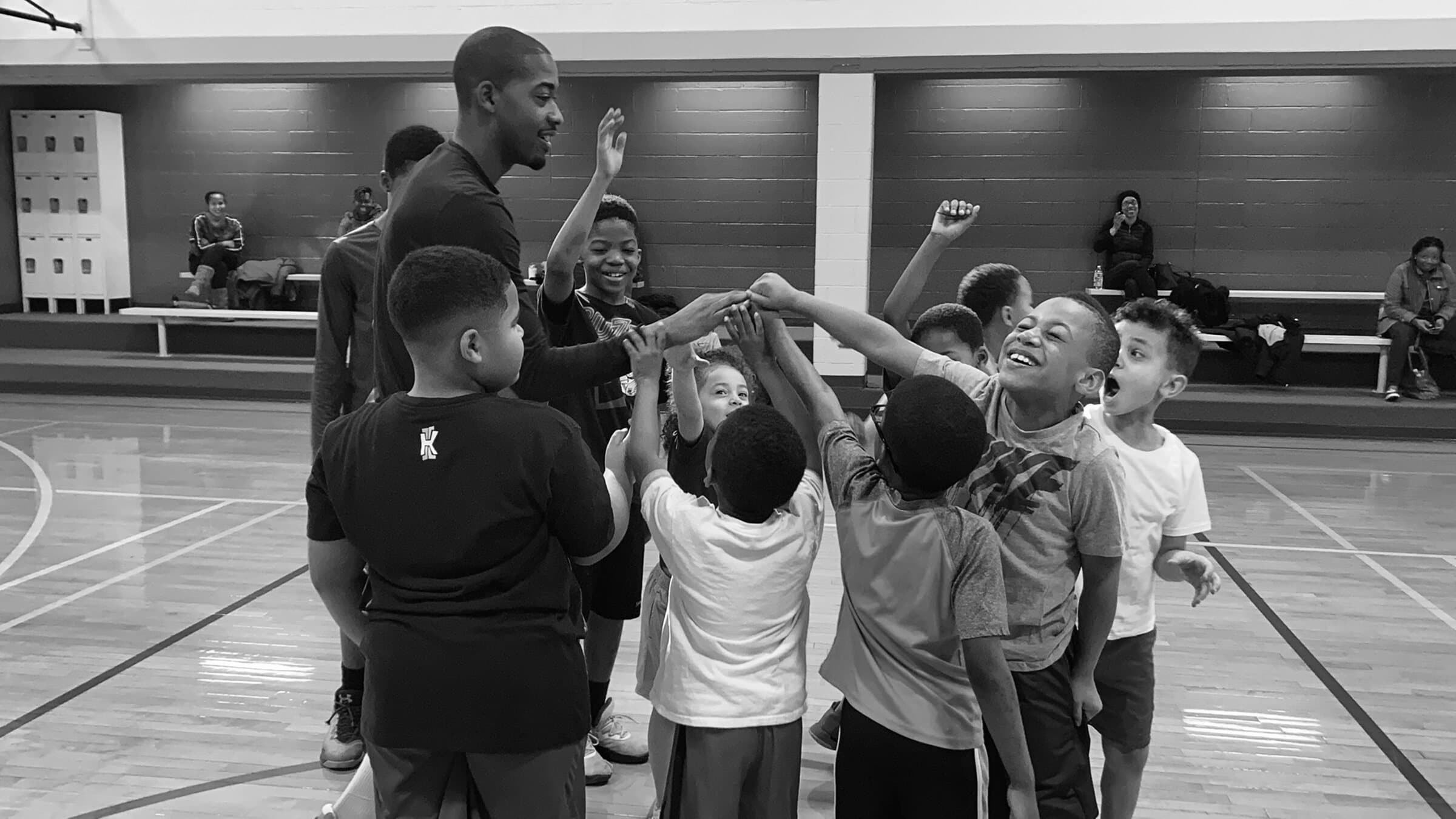 Rashad Petty and young athletes bringing their hands together after a community basketball session