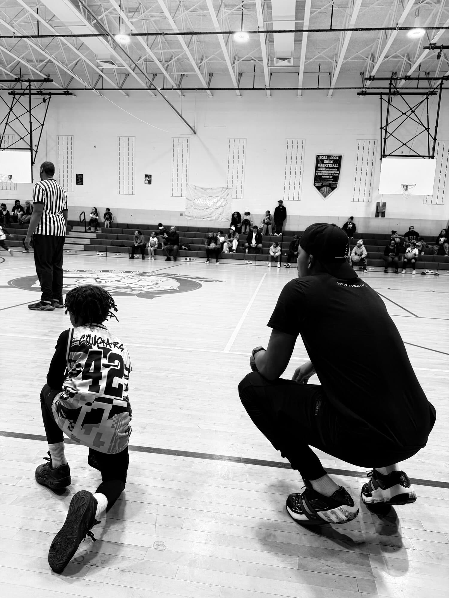 Rashad Petty seated courtside with a young athlete during an inclusive-adaptive basketball session